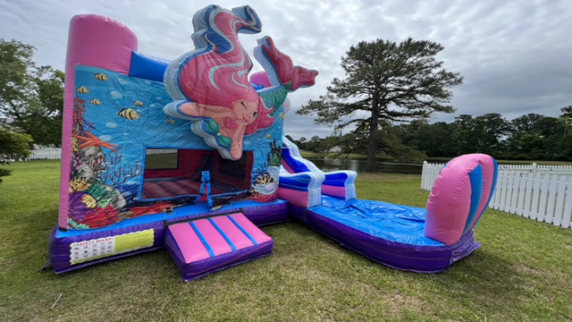 Mermaid Princess Bounce House rental Wilmington NC—a magical mermaid and ocean-themed inflatable with an exciting slide, set on grass near a white fence and trees under a cloudy sky. Bounce house rentals Wilmington NC - Funtime Inflatables NC