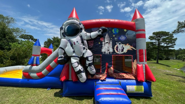 Set up outdoors under a partly cloudy sky, the Astronaut Bounce House features a large astronaut, rocket decorations, and an exciting slide—making it the ideal bounce house & slide combo rental for Wilmington NC families searching for an out-of-this-world event experience. Bounce house rentals Wilmington NC - Funtime Inflatables NC