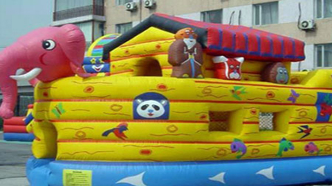Set outdoors near a building, the vibrant Noahs Ark Bounce House features colorful ark-shaped inflatable play with animal and human figures—including a pink elephant head and painted animal faces—making it a fun bounce house rental Wilmington NC families will love for their next event. Bounce house rentals Wilmington NC - Funtime Inflatables NC