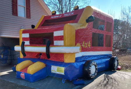 A large MONSTER TRUCK bounce house from Funtime Inflatables NC, shaped like a truck and decorated with “HUMMVY TRUCK” and “4x4,” in bright red, yellow, and blue—ideal for anyone looking to rent a monster truck bounce house in Wilmington, NC. Bounce house rentals Wilmington NC - Funtime Inflatables NC